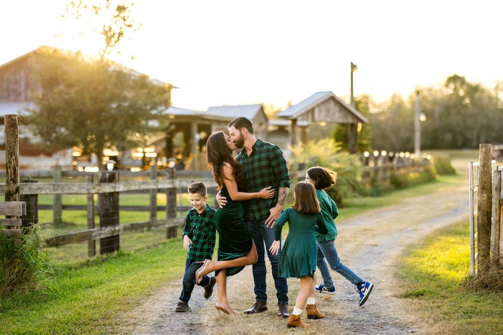 Family members walk together along a rustic country path at sunset with wooden fences and trees in the background.