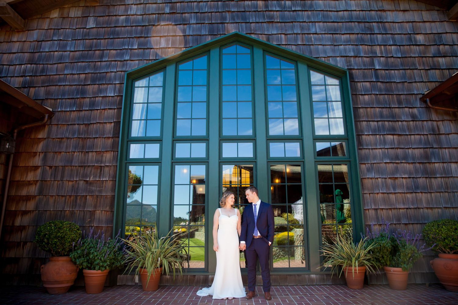 Rustic brick building exterior with arched windows and potted plants along a covered walkway.