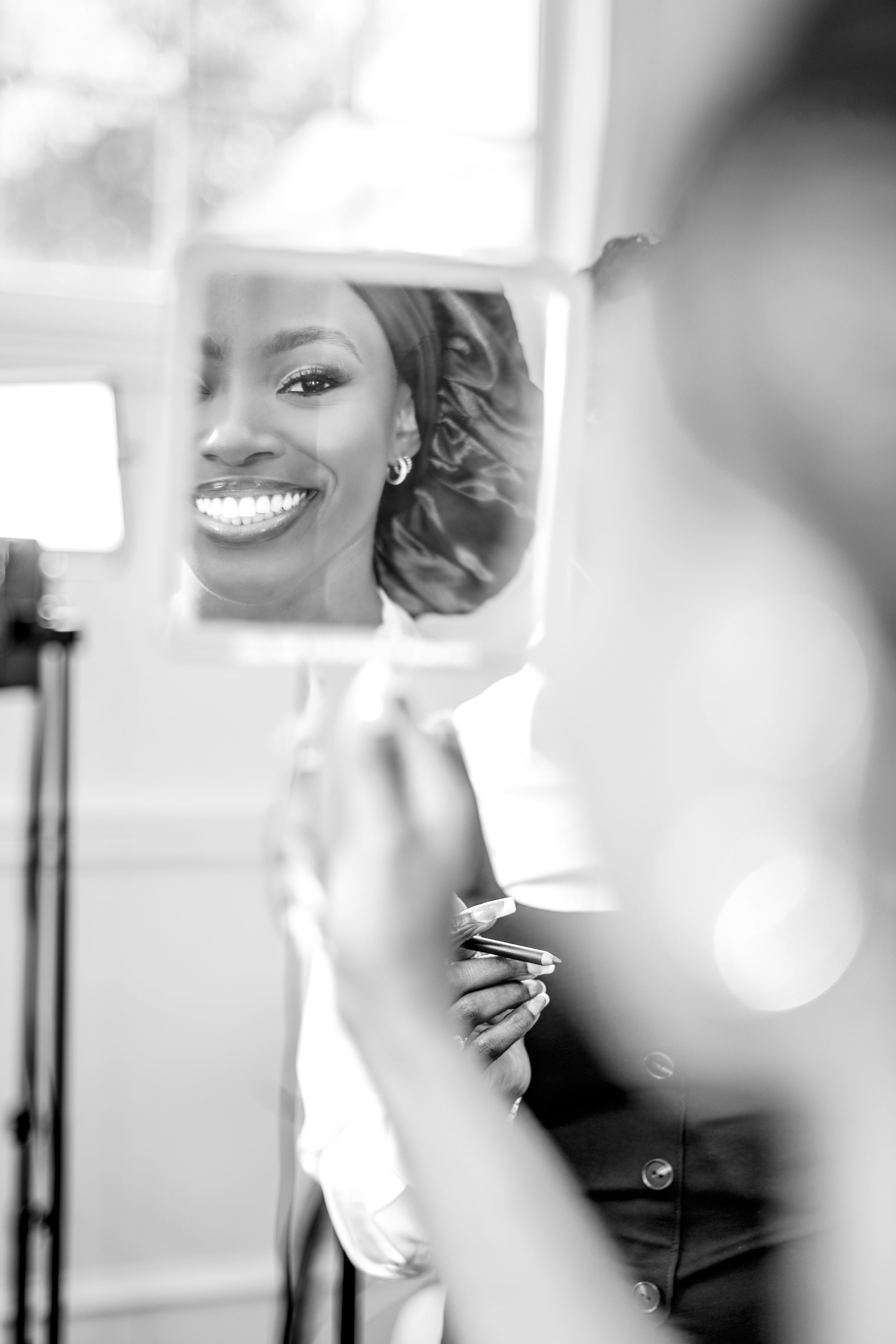 A reflection in a mirror shows a bright smile and manicured nails in an elegant black and white portrait.