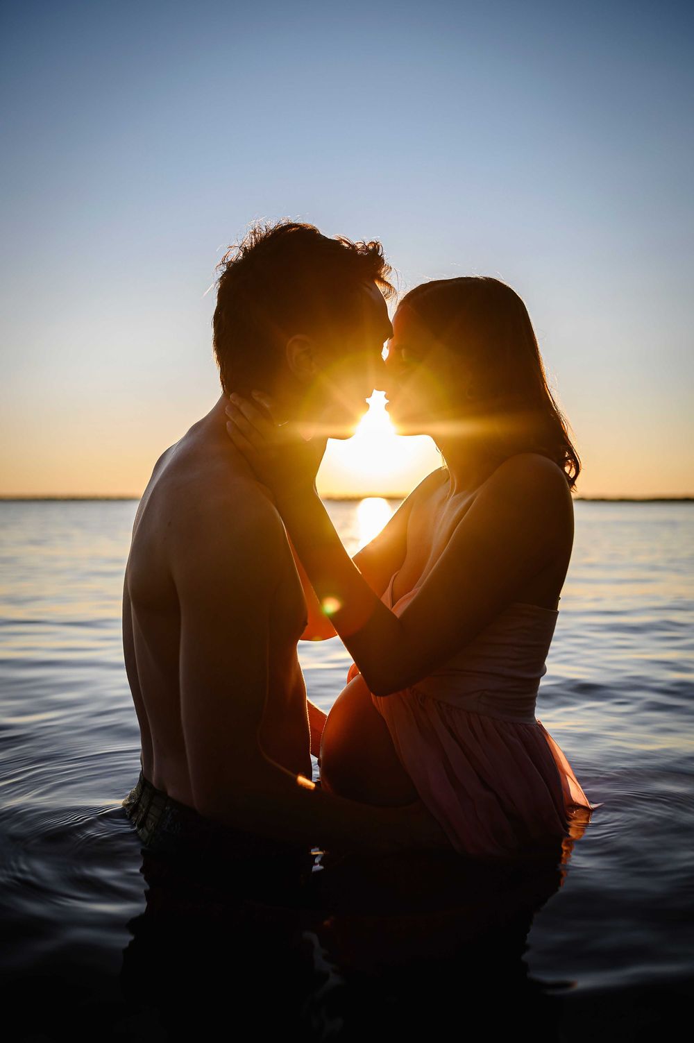 Silhouette of a romantic couple in water at sunset sharing an intimate moment.