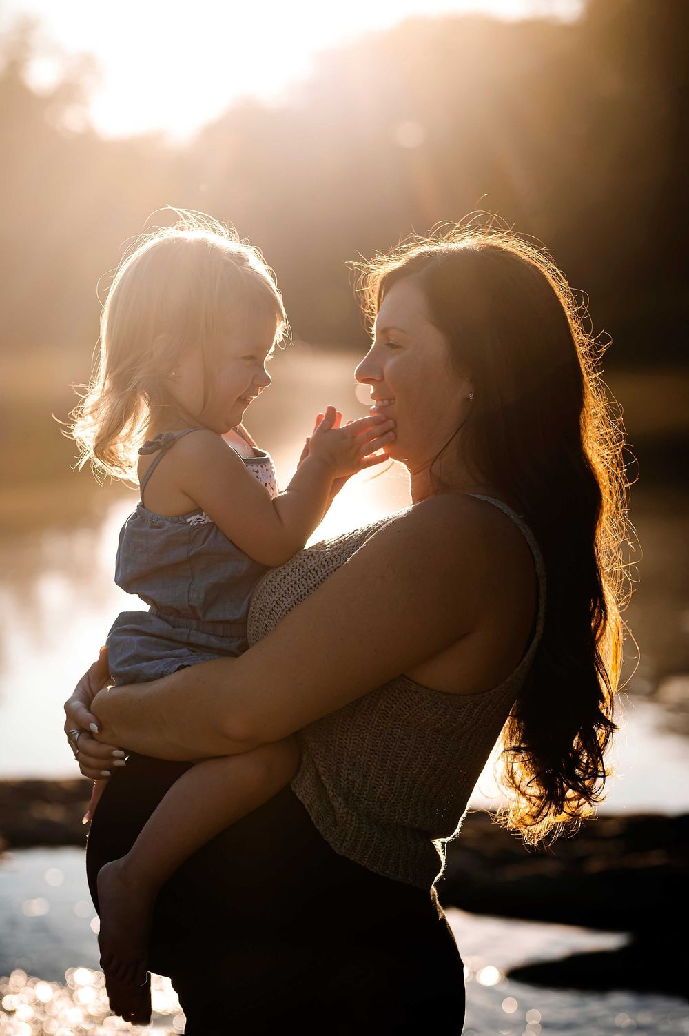 Tender moments captured in silhouette during golden hour by the water.