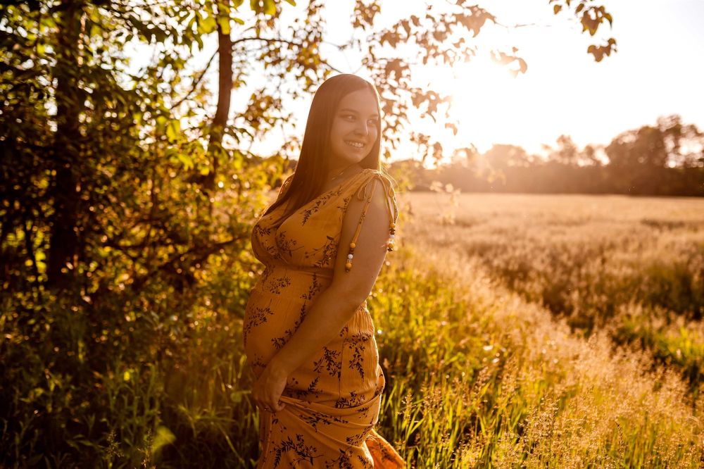 Golden hour maternity session in a field with sunlit autumn foliage.
