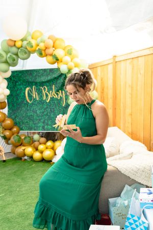 A festive baby shower celebration with emerald green decor, gold balloons, and a person in a flowing green dress.