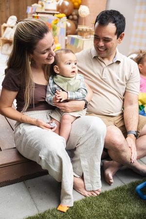 Family sitting together on floor with baby enjoying playful moments on artificial grass mat.