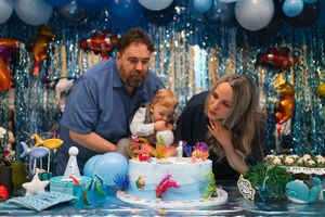 People gather around a festively decorated table with blue and white balloons and party decorations for a celebration.
