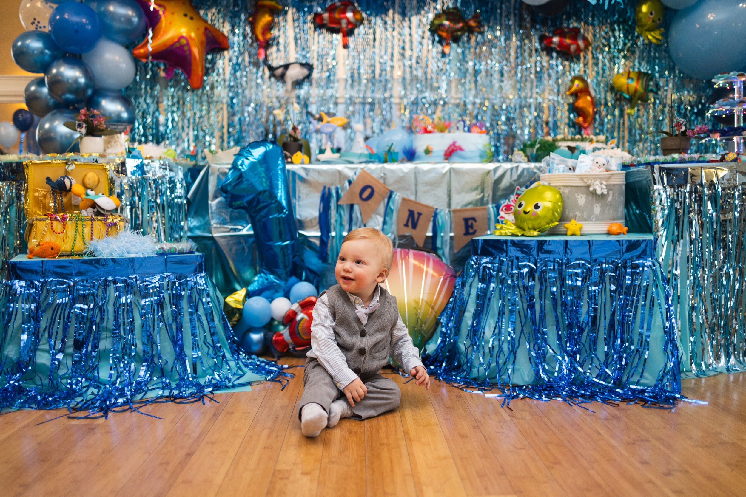 A birthday party setup with blue tablecloths, colorful balloons, and decorations in a festive indoor space.