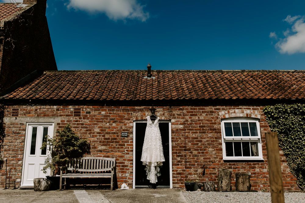 Rustic brick buildings with white windows and tiled roofs line up against a bright blue sky in a historic architectural view.