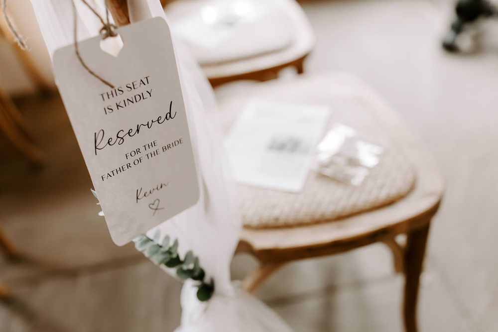 A reserved wedding table card with elegant calligraphy sits beside white decor and delicate greenery.
