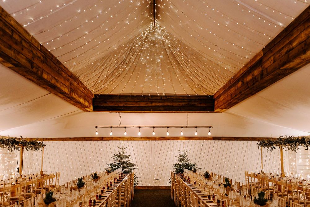 Rustic barn wedding venue interior with exposed wooden beams and twinkling string lights creating a romantic atmosphere.