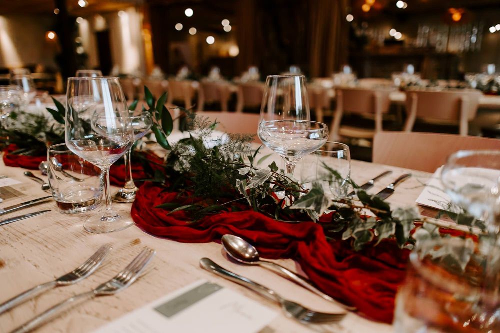 Elegant wedding table setting with red velvet runner and greenery garland centerpiece in romantic candlelit venue.