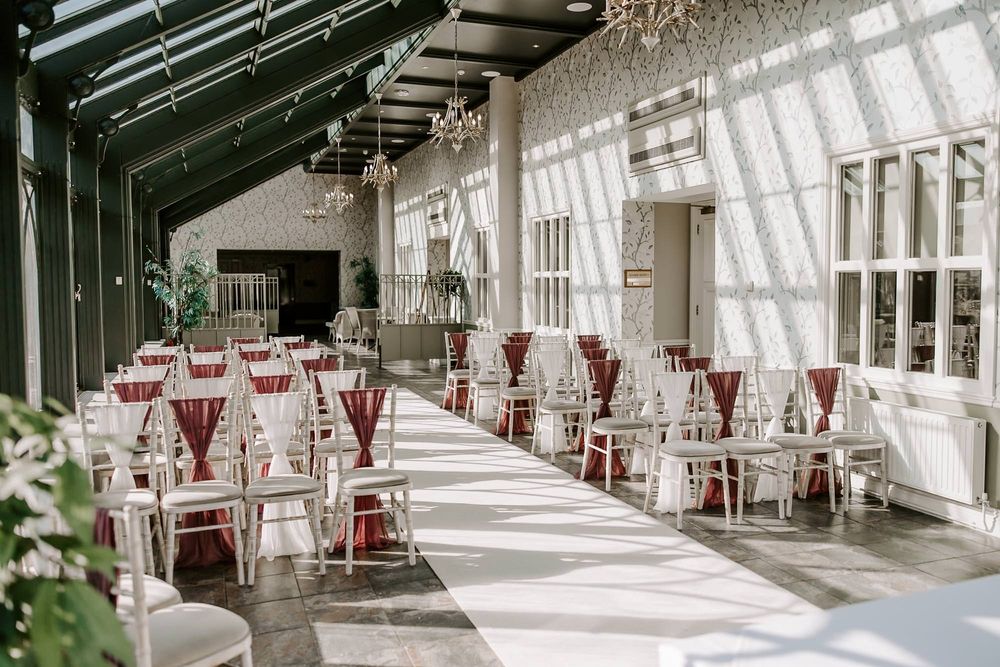 Sunlit indoor venue with white walls and red chairs arranged in rows for an elegant event space.