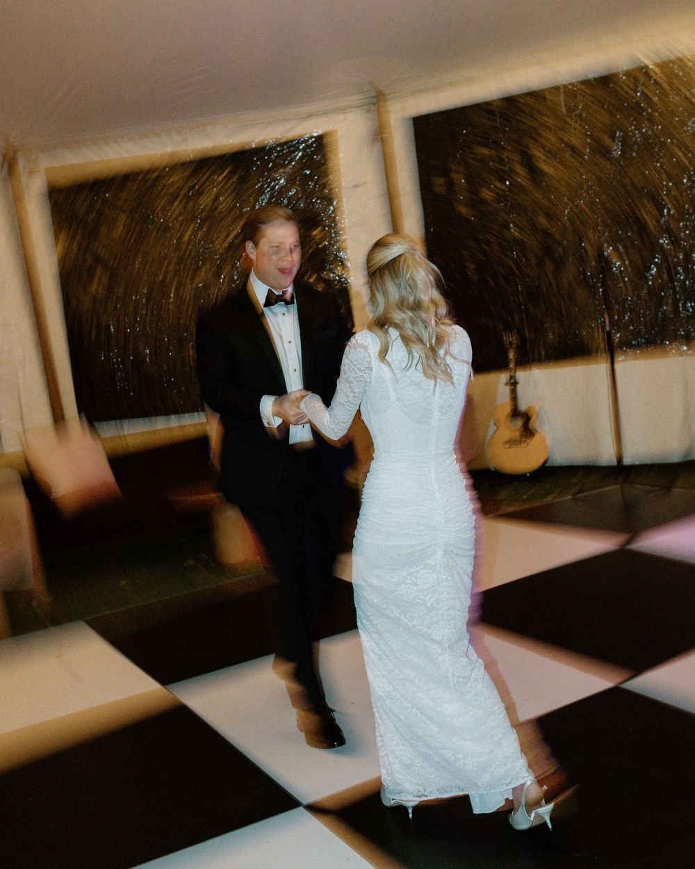 A couple dancing together on a black and white checkered dance floor at their wedding reception.