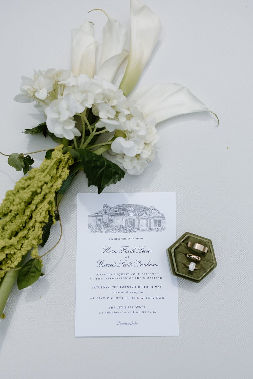 Elegant wedding stationery with white floral arrangements, green amaranthus, and a hexagonal ring box displayed on white surface.