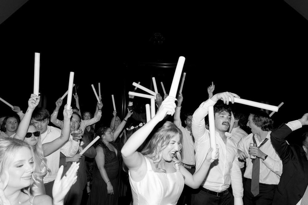 A crowd raises illuminated wands in unison during a darkened indoor celebration.