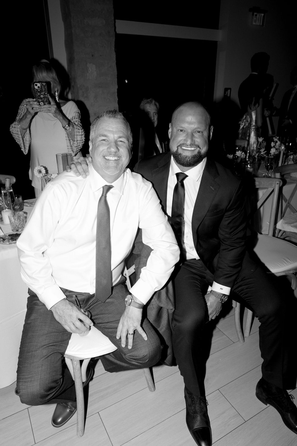 Four black and white photos show people in formal attire sitting and laughing together at an event.