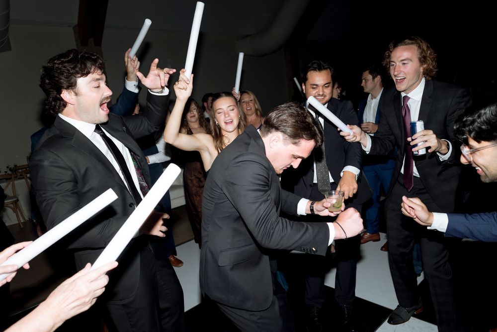 People in formal attire hold glowing light sticks during a celebratory event in a dark room.