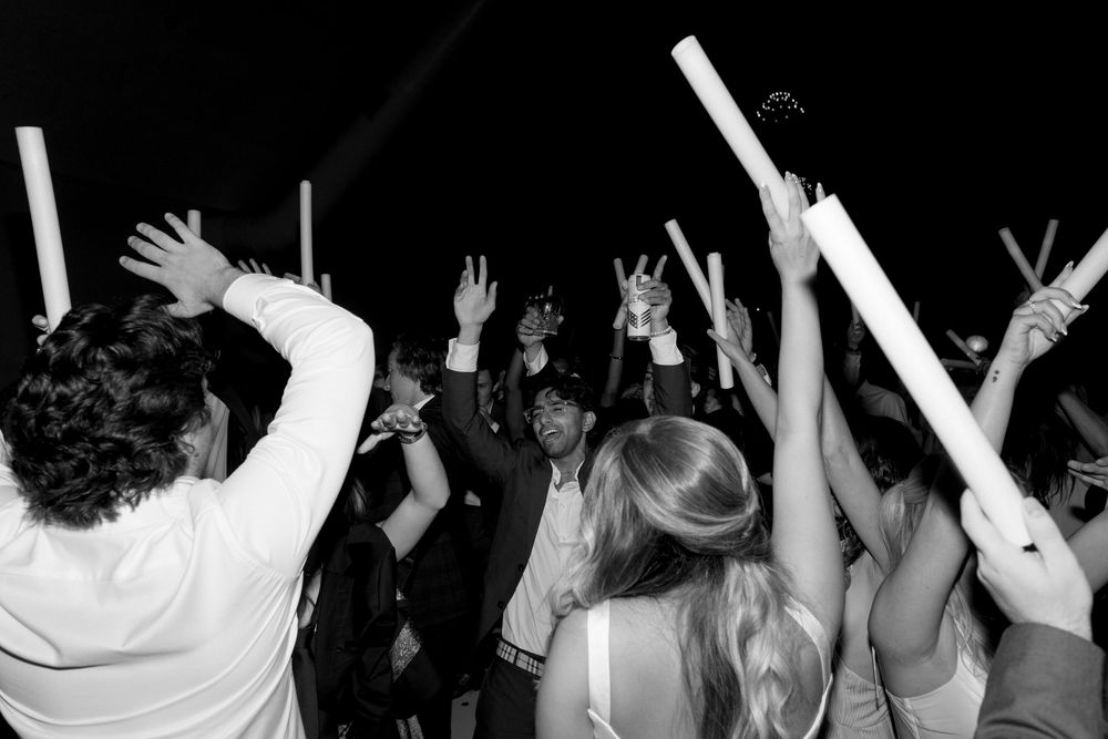 Black and white photo showing an energetic concert crowd with raised hands and silhouettes against dark lighting.
