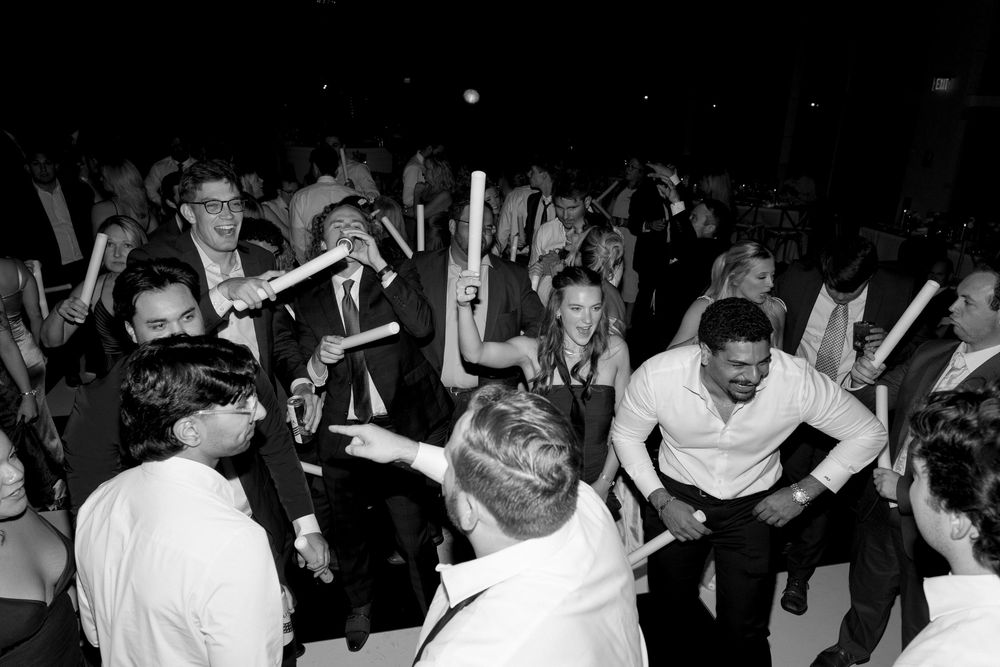 Monochrome image of a lively crowd dancing and celebrating at a music event with hands in the air.