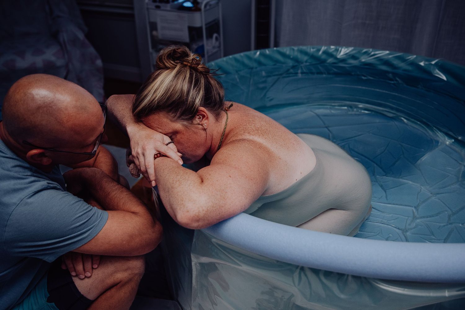 A couple embraces in a romantic moment while swimming in a pool at dusk.