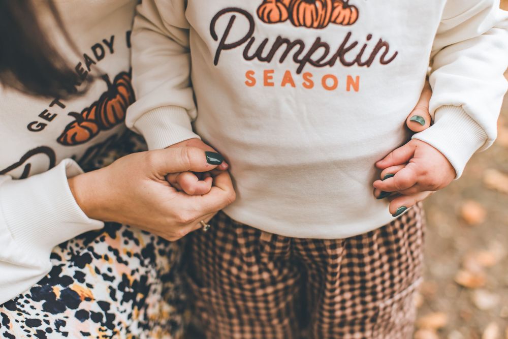 Couple holding hands and walking through autumn pumpkin patch with fall decor and white t-shirts.