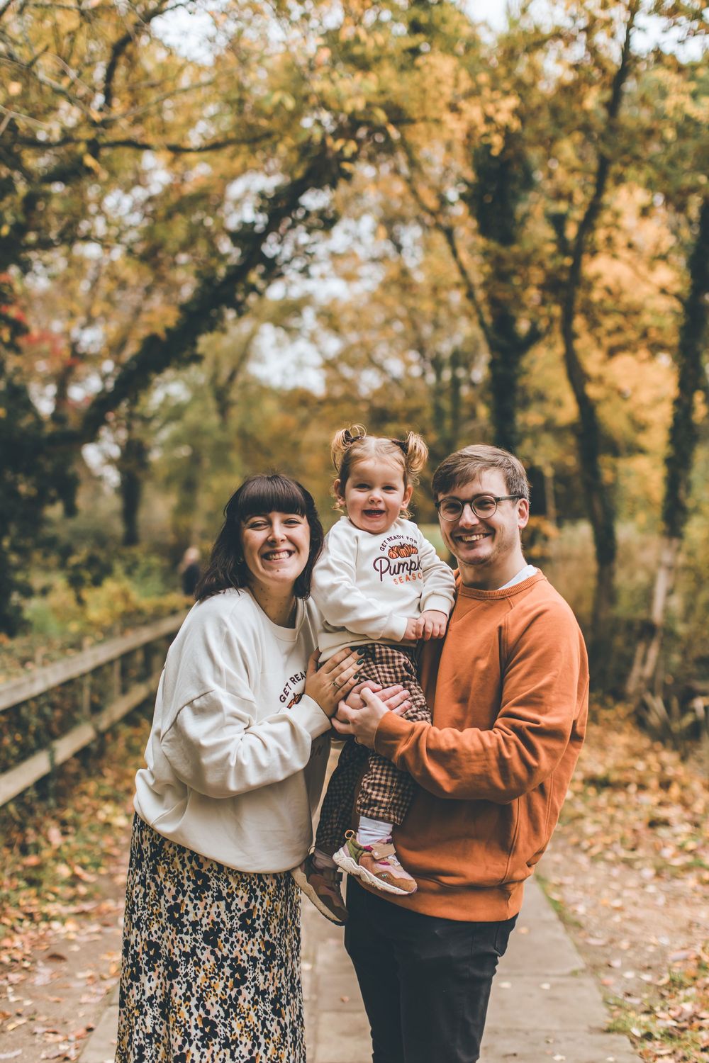 A family group enjoys a playful autumn moment together surrounded by golden fall foliage.