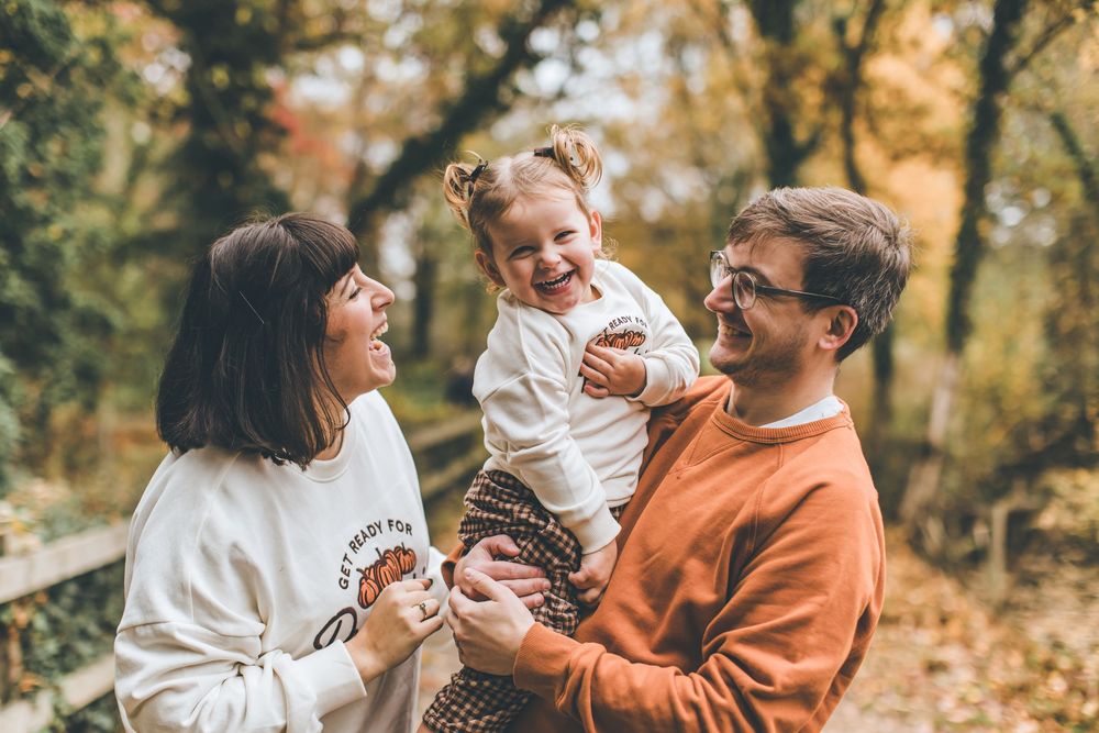 Happy family enjoying a playful autumn photoshoot together in a park with golden fall foliage.
