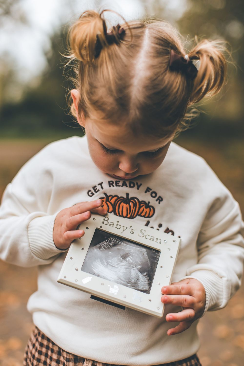 A series of photos showing a small sonogram print being held and kissed against a white sweatshirt in autumn.