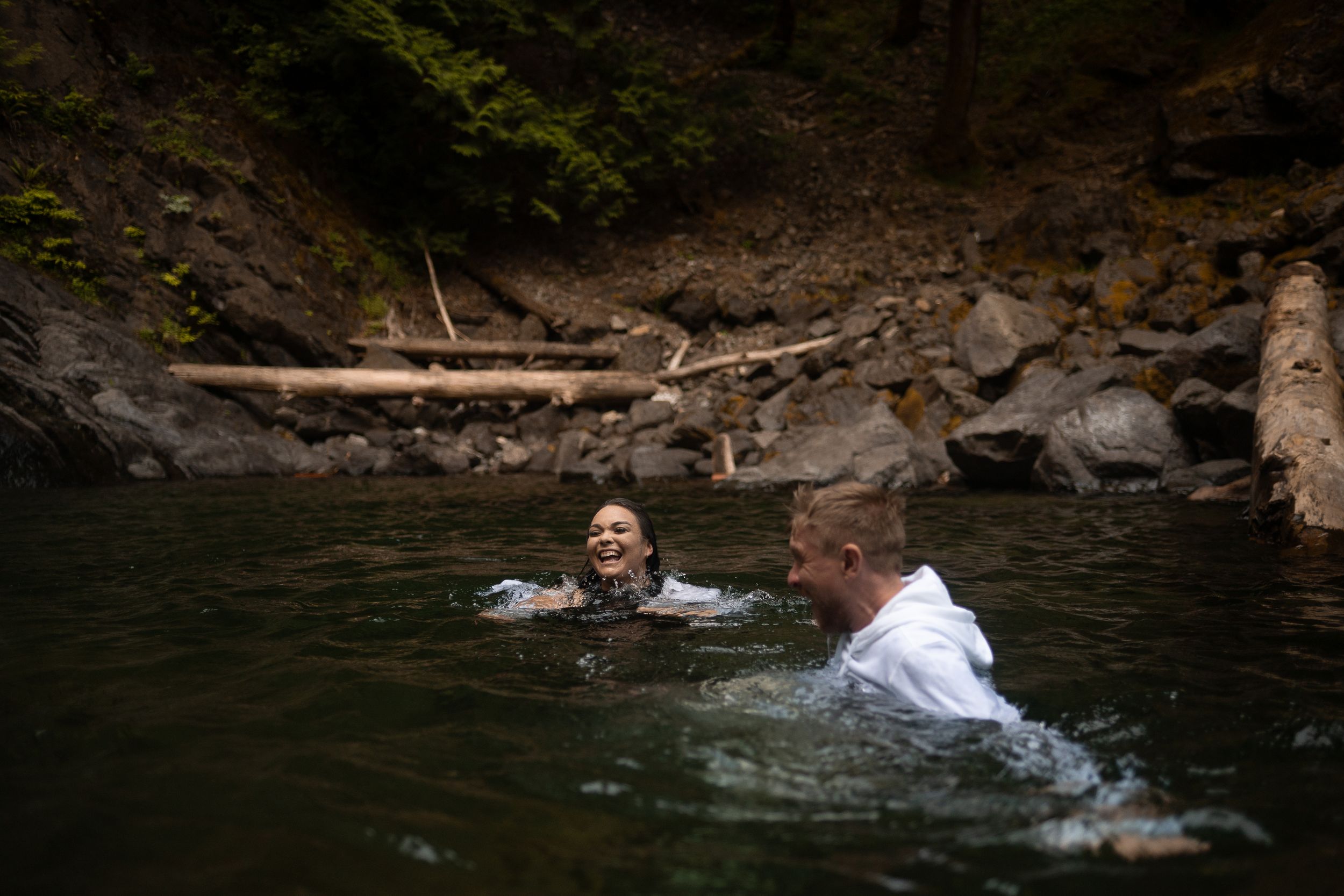 A couple swims in the pool at the base of a waterfall near Olympic National Park.