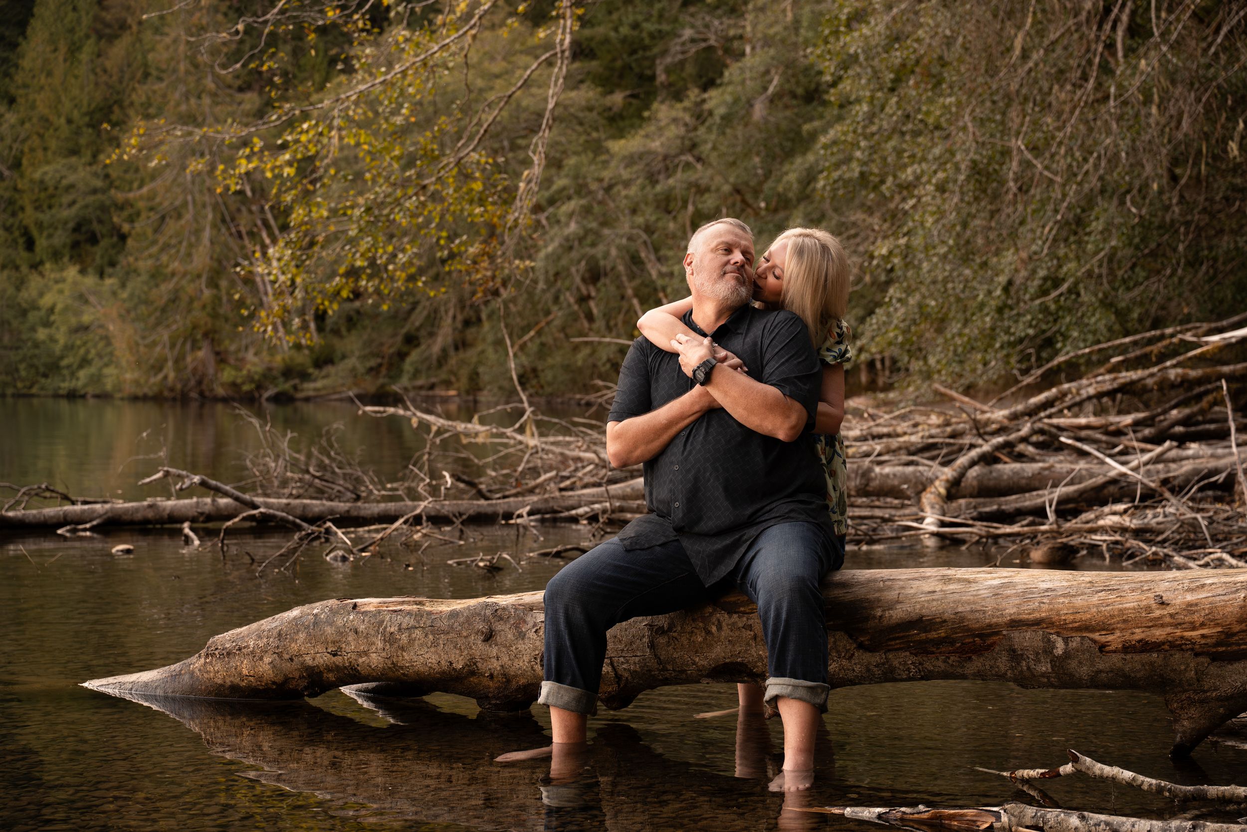 An older couple embraces while sitting on a log at lake Crescent in Olympic National Park.