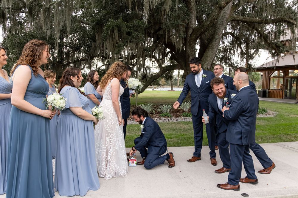 Wedding party in dusty blue bridesmaid dresses and navy suits gather outdoors for formal photos.