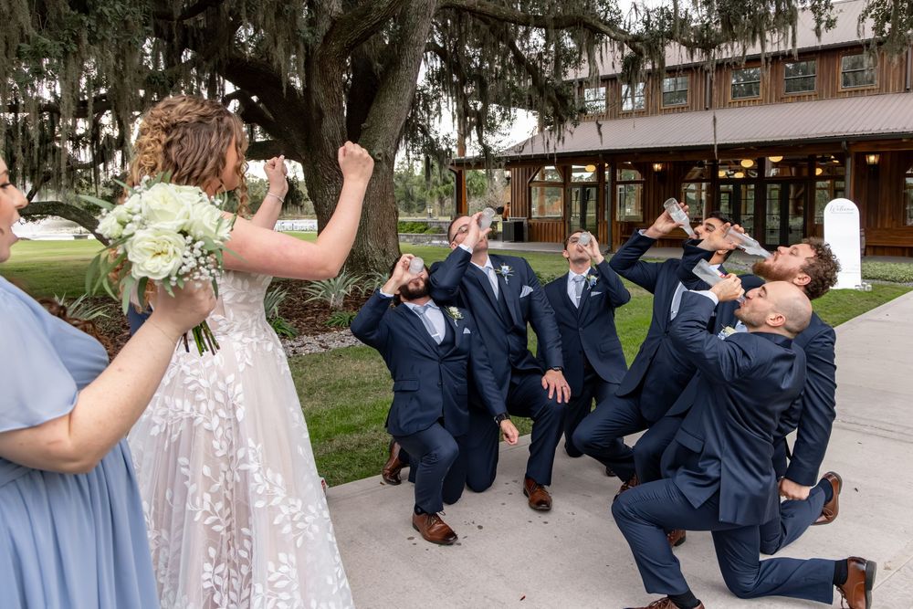 Wedding party in navy suits and mix of blue and burgundy dresses pose playfully on outdoor walkway.