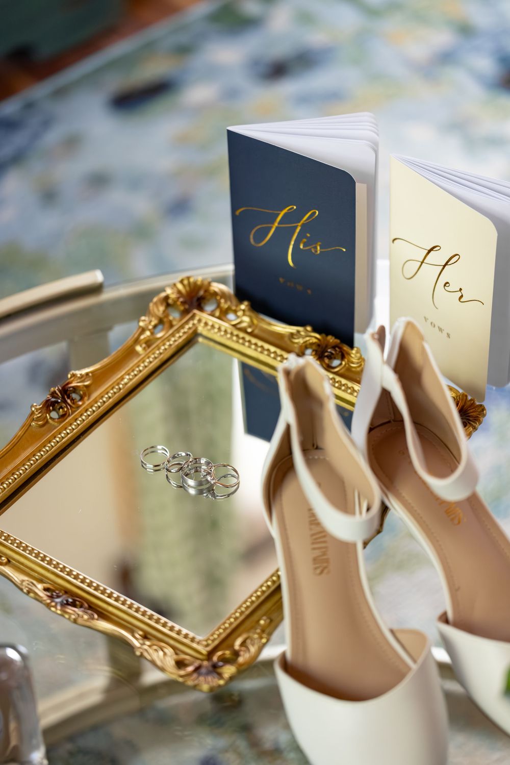 Wedding details featuring elegant nude heels, wedding rings, and a decorative gold-framed mirror arranged artistically.