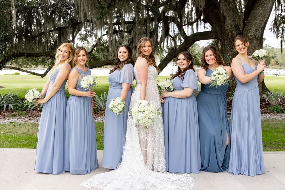 Wedding party in light blue bridesmaid dresses poses together outdoors under Spanish moss draped trees.