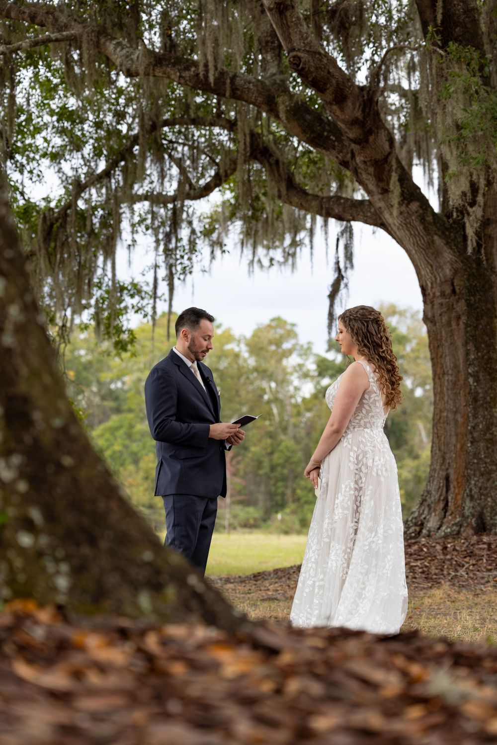 A couple stands beneath a Spanish moss-draped oak tree during an intimate wedding ceremony moment.