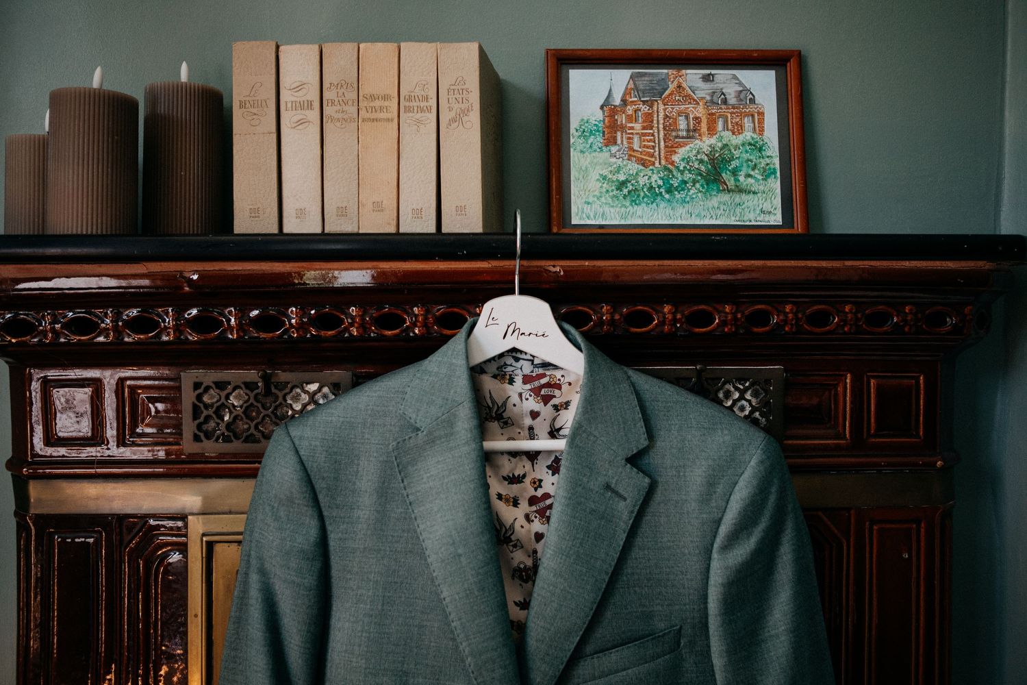 Gray groom's suit jacket with patterned lining displayed on hanger over ornate wooden mantelpiece with books.