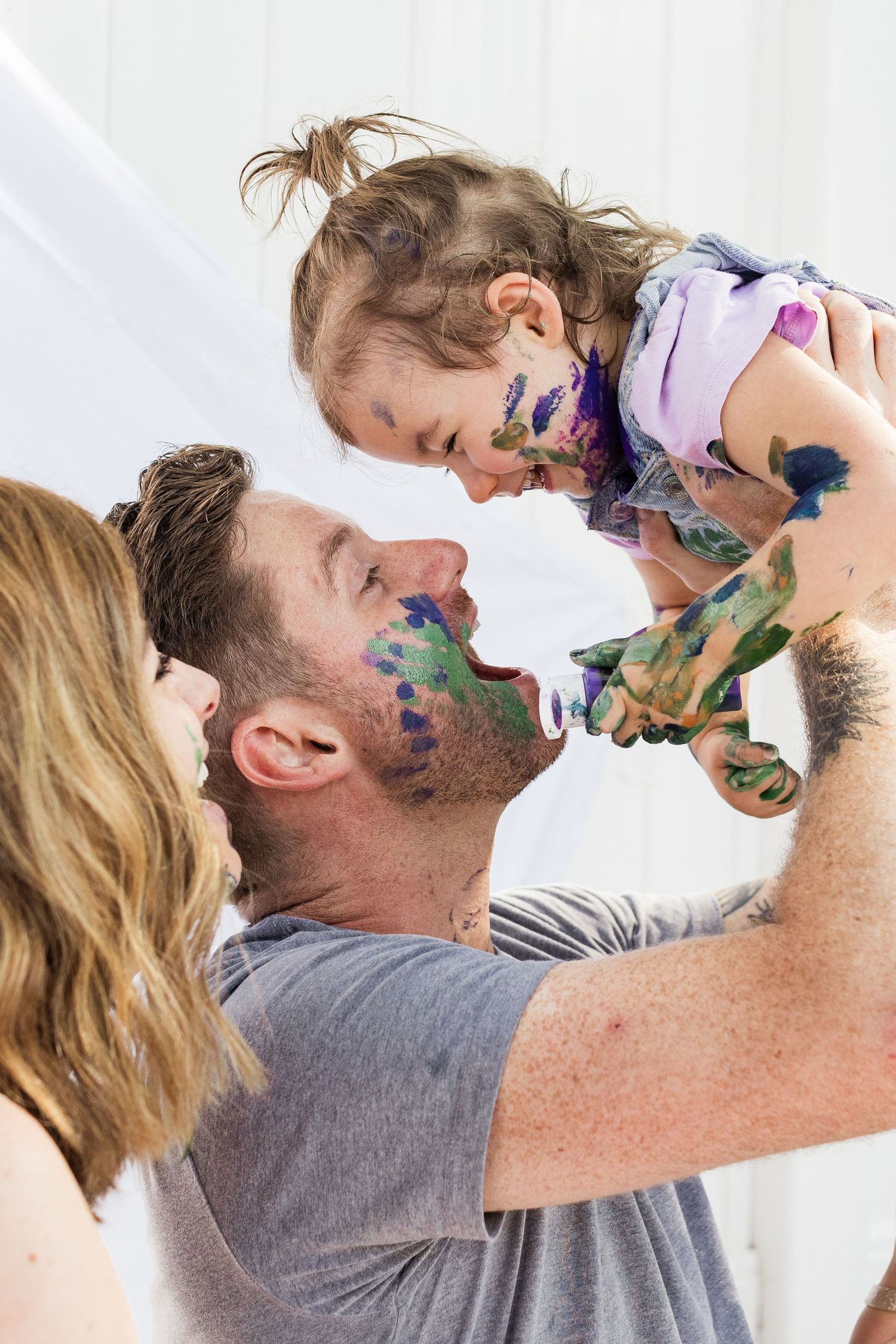 Playful family moment with paint-covered faces in a bright indoor setting.