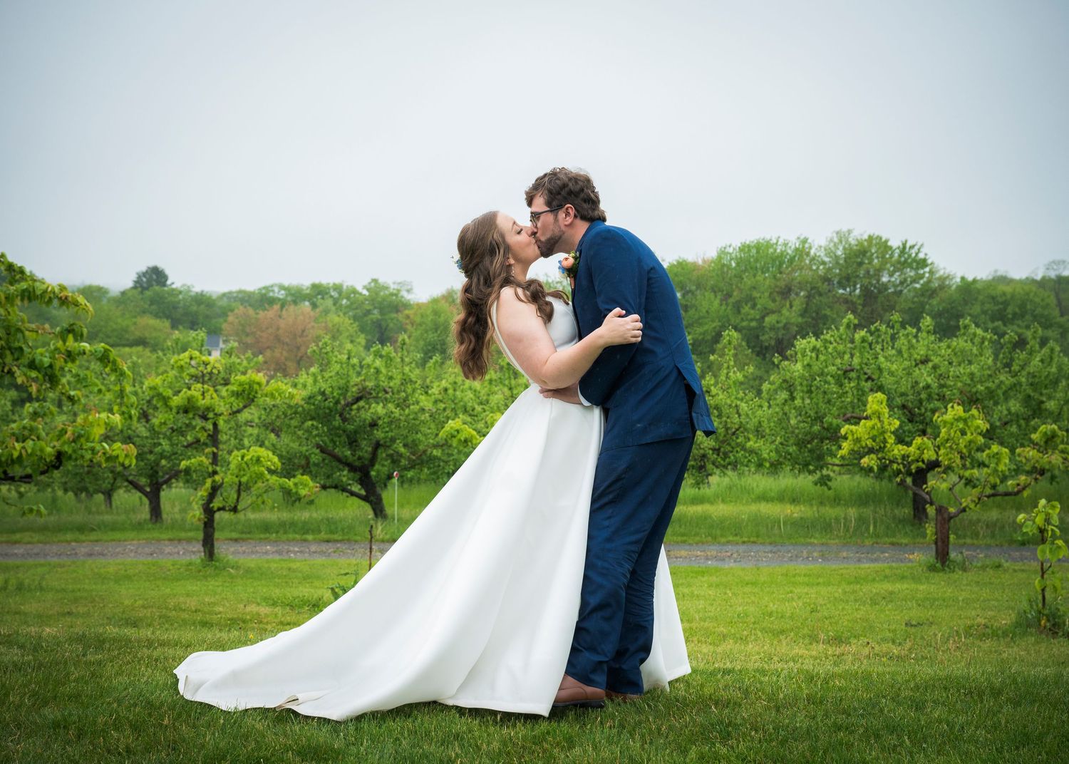 A romantic wedding couple shares a kiss in a lush green orchard on their special day.