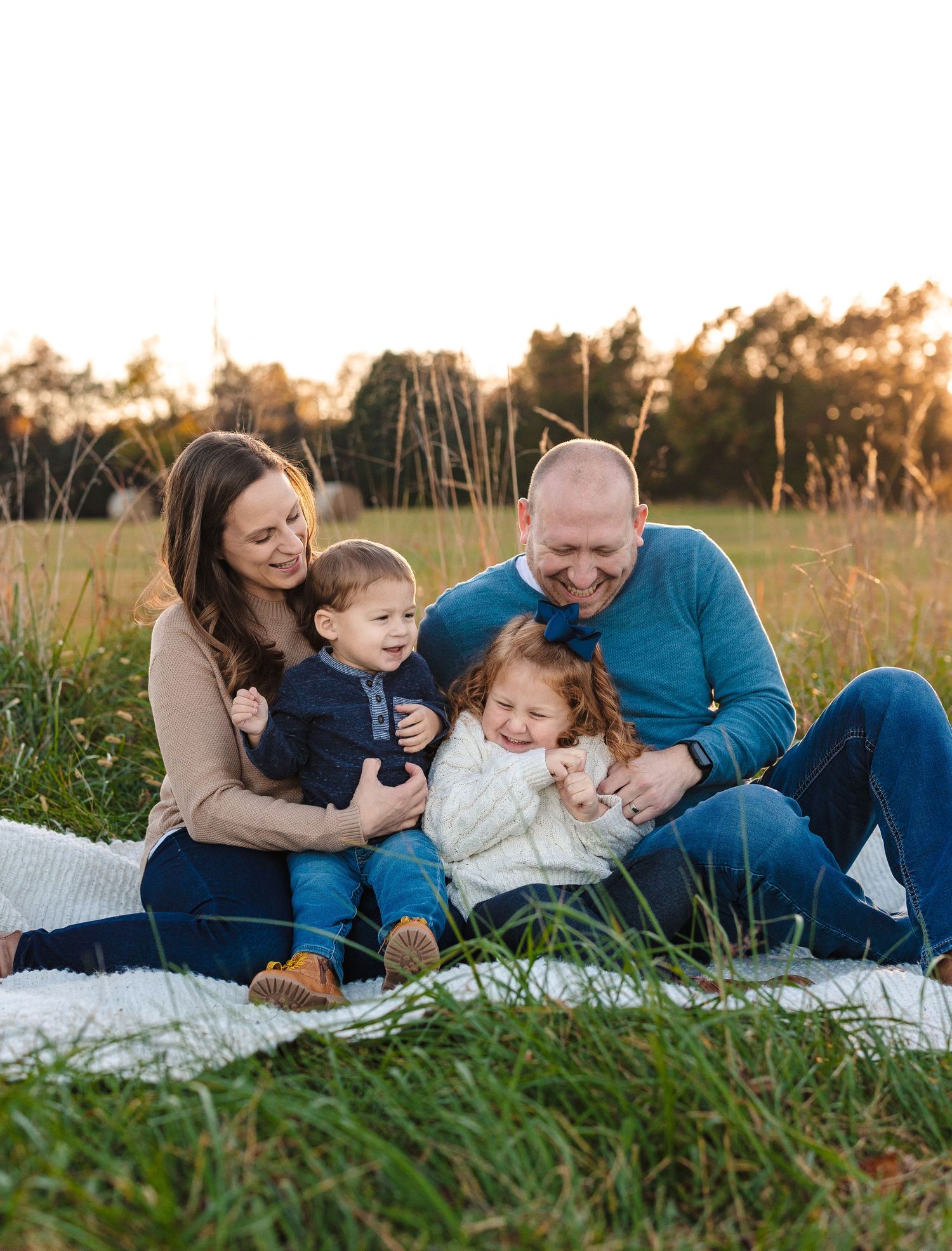 Family enjoying quality time together while sitting on a blanket in a grassy field at sunset.