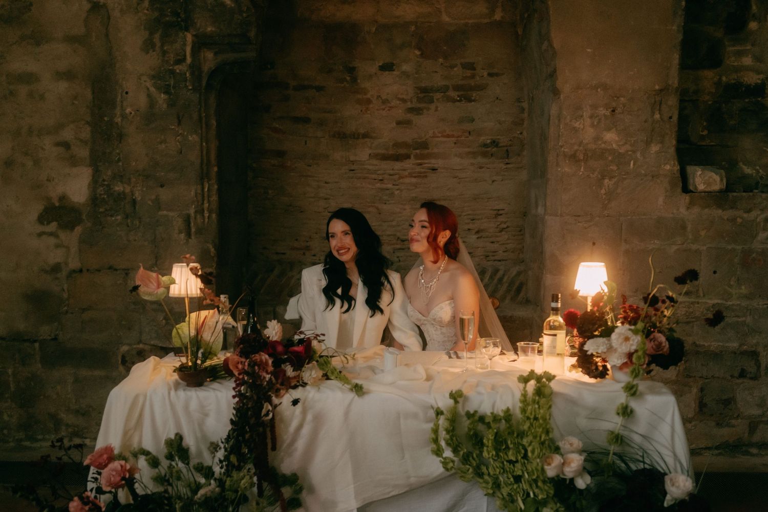 A candlelit wedding reception table in a rustic stone building with elegant floral arrangements and glowing ambiance.