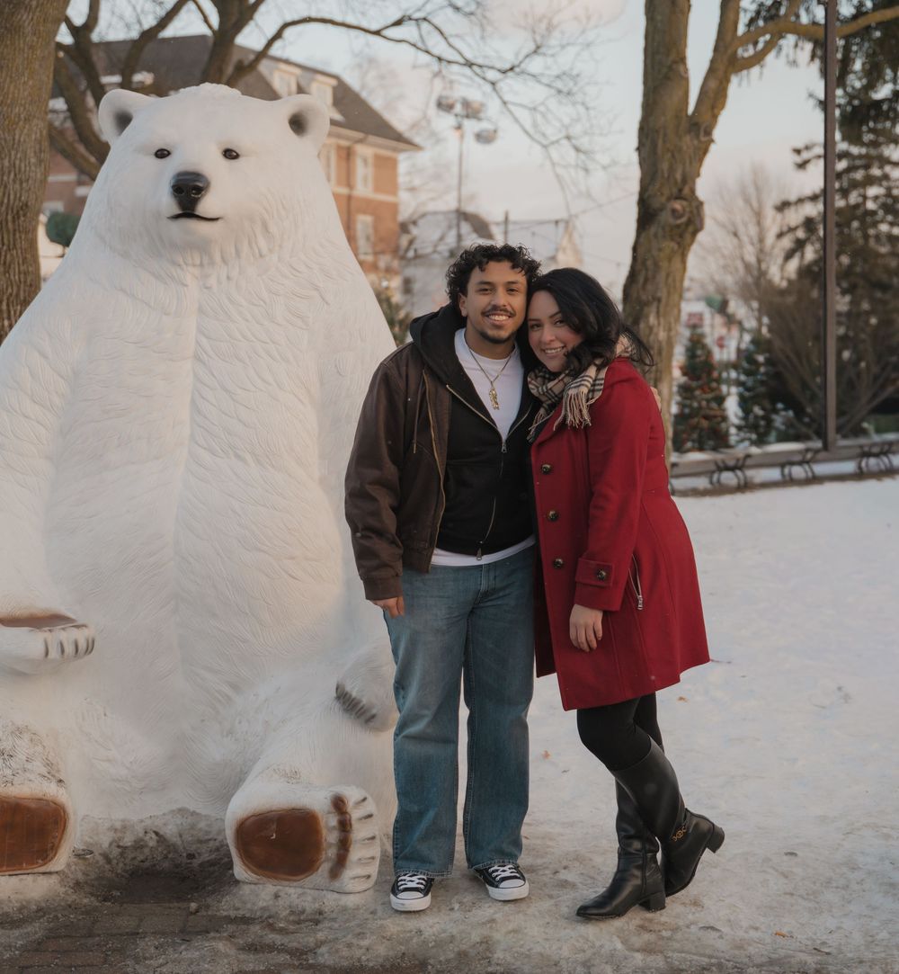 A couple poses next to a large white polar bear statue in a snowy winter setting.