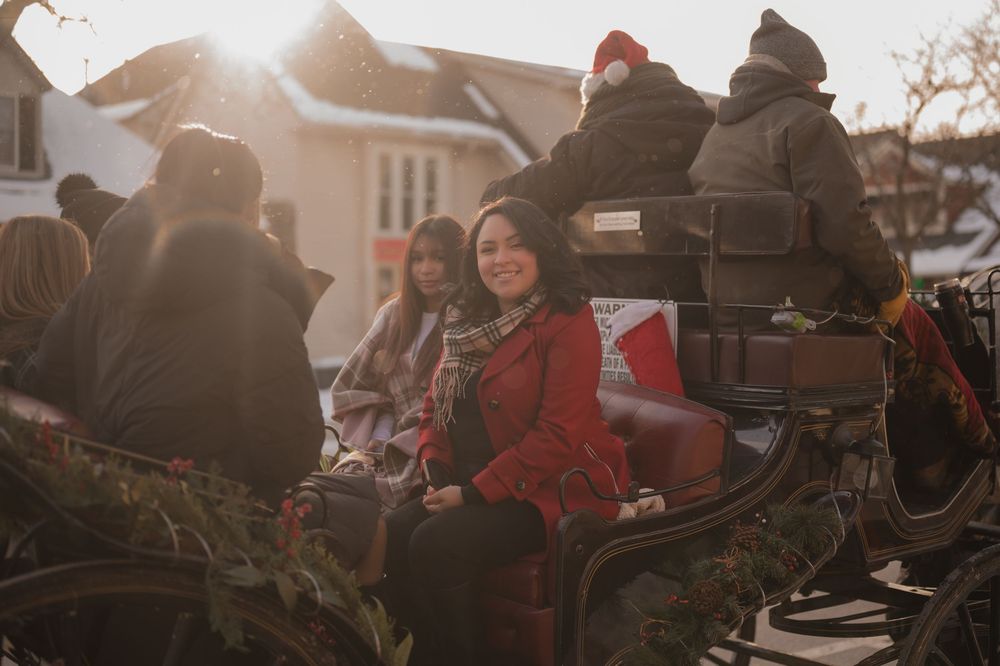 A group of people ride horses in formation during a winter parade event as sunlight streams through the trees.