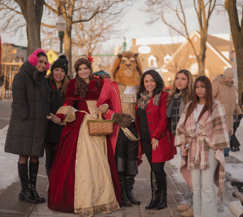 A group of people in winter coats gather outdoors during a sunset photoshoot in snowy conditions.
