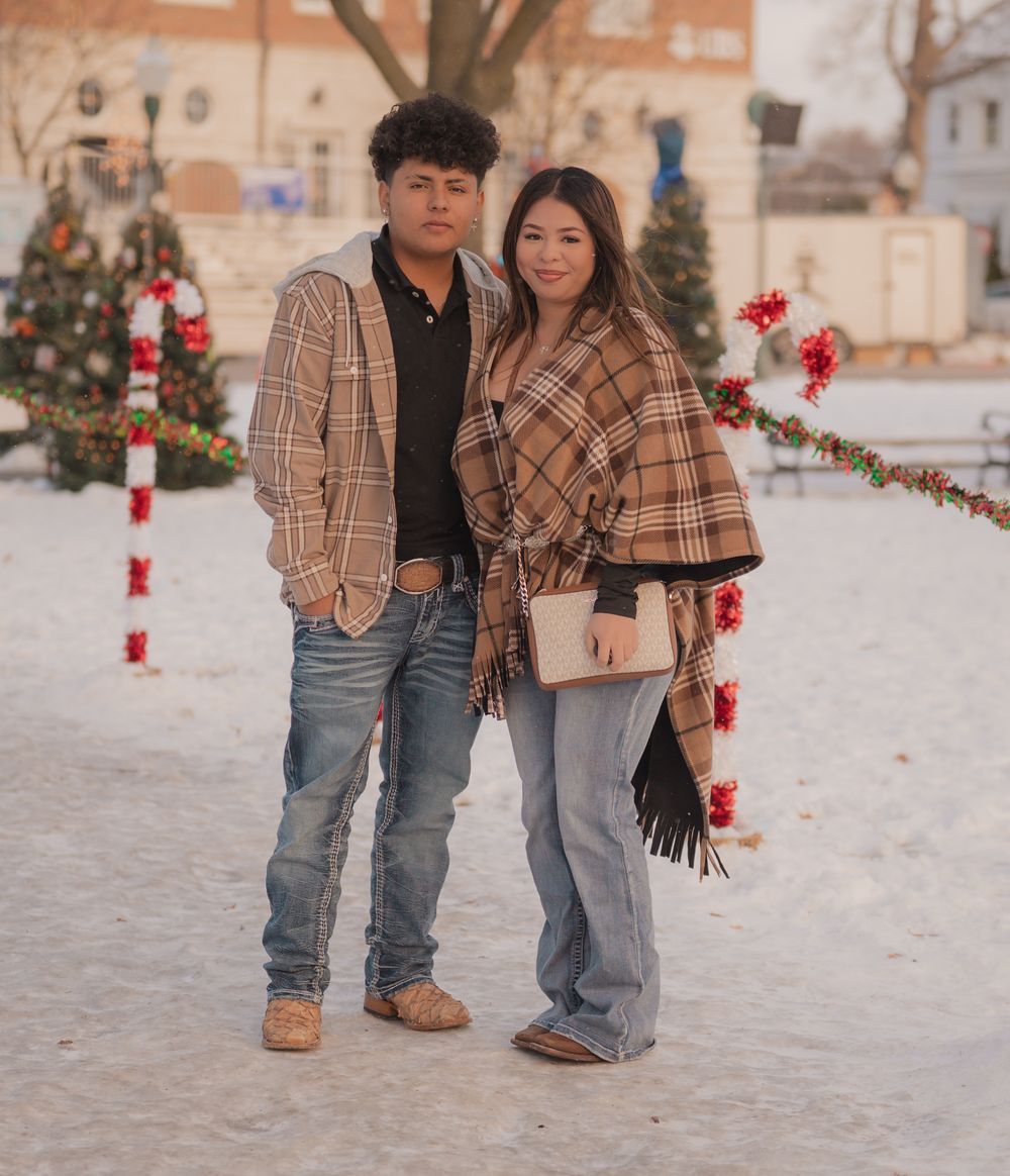 A couple in plaid winter outfits poses together near festive candy cane decorations and Christmas ornaments.