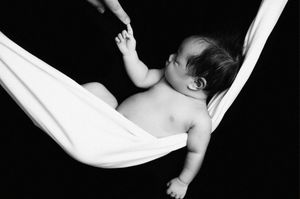 Black and white photo of baby resting peacefully in white fabric hammock.
