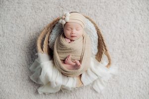 Newborn baby sleeping peacefully wrapped in white and beige textiles on textured background.