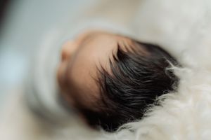 Side view of sleeping newborn with dark hair wrapped in soft white blanket.