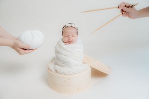 Gentle hands placing soft white blankets in a woven basket for newborn photography setup.