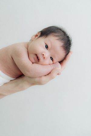 Minimalist newborn portrait with baby cradled in hands against white background.