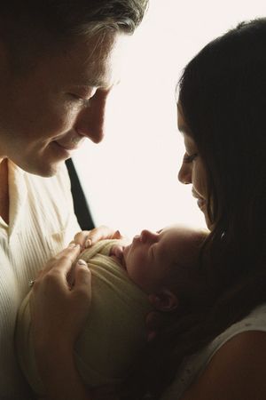 Intimate silhouette of parents gazing lovingly at their newborn baby in warm lighting.