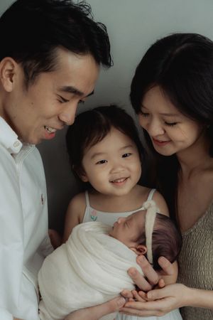 Joyful family moment with parents cradling their newborn while toddler smiles.